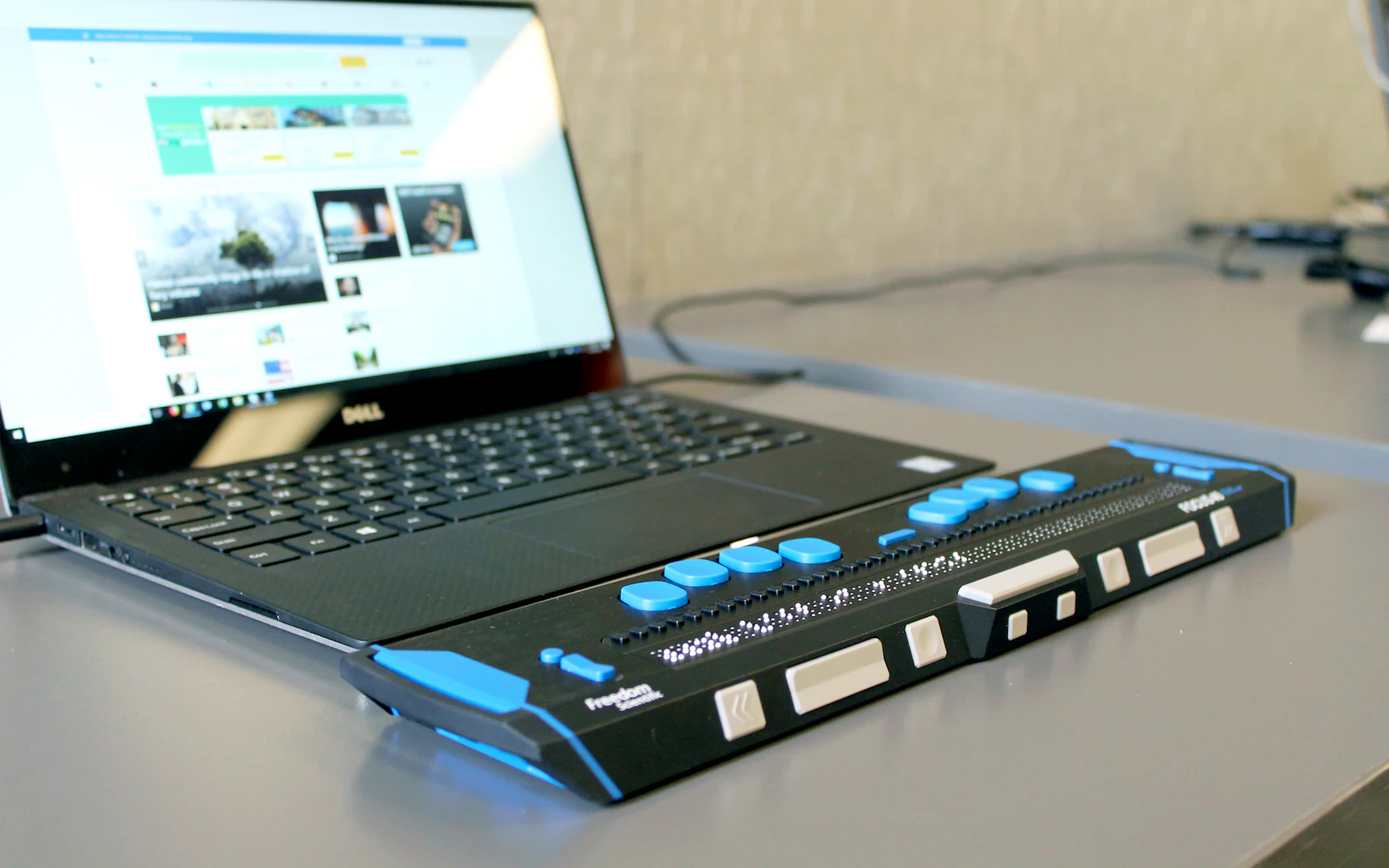 A refreshable braille display in front of an open laptop