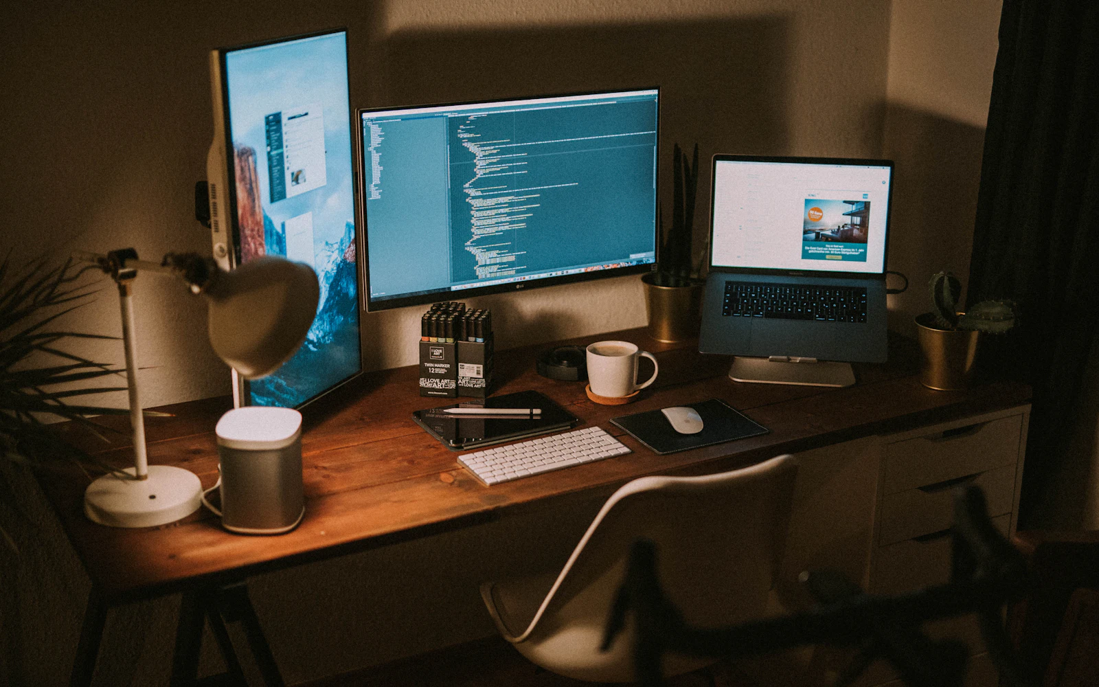 Monitors and a laptop glowing in a dark room