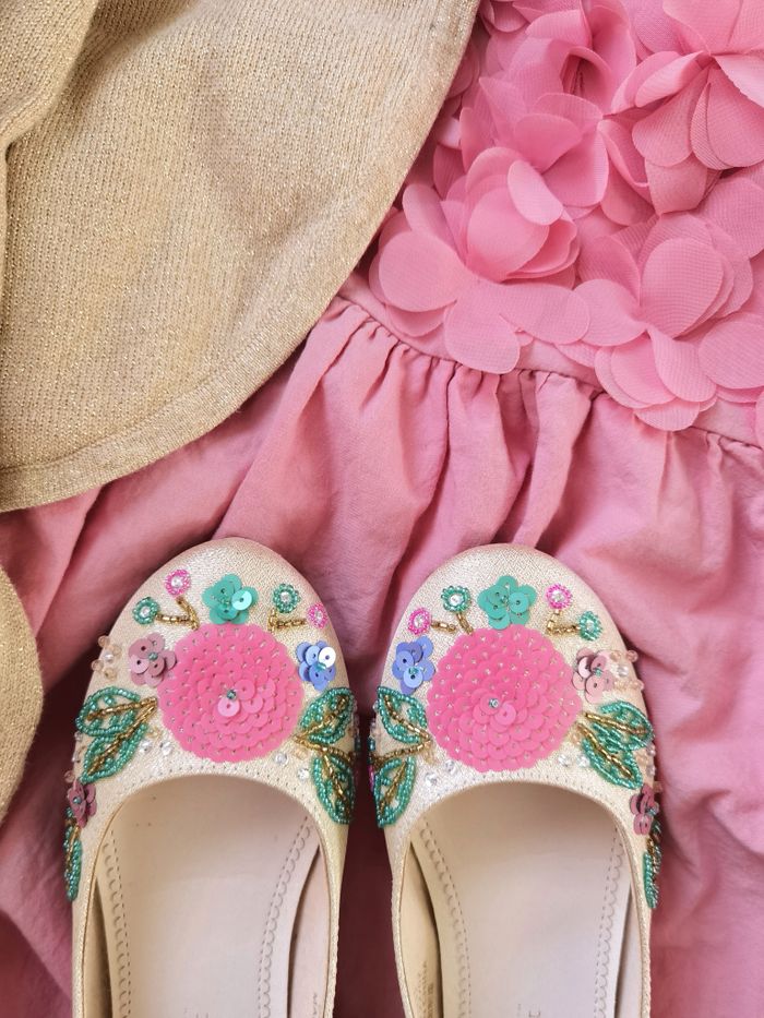 Cecily cream ballet flats embroidered with pink and turquoise beaded flowers, resting on gathered pink fabric.