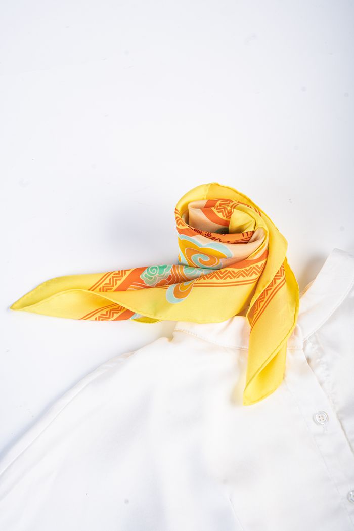 Isla silk scarf in a yellow and orange print, twisted into a loop on a white shirt.
