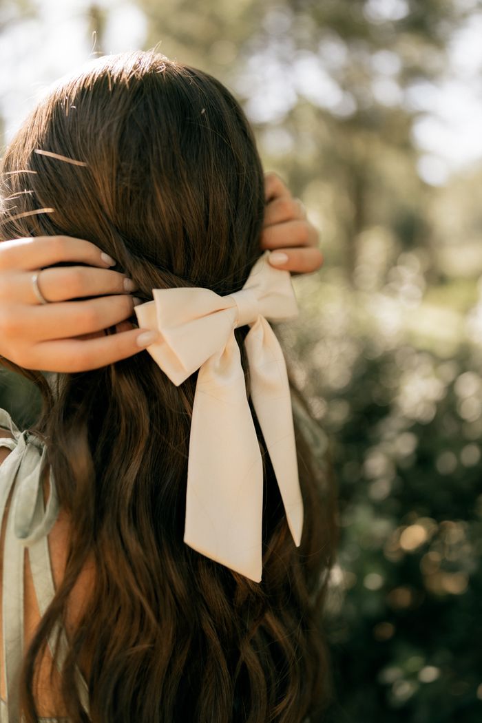 The satin bow barrette from the Posy set, clipped into long chestnut hair.