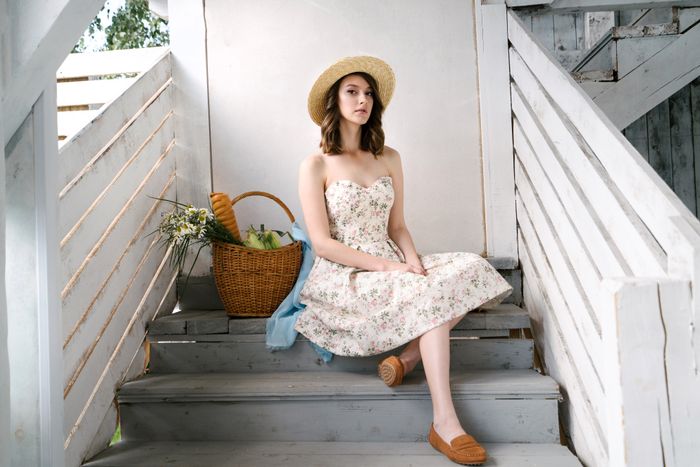 Clementine sweetheart sundress in pink-and-cream florals, styled with a straw hat on weathered white steps beside a basket of daisies.