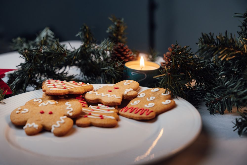 Iced gingerbread cookies on a white plate beside a lit candle and dark fir branches, on a table in a dim, cosy room.