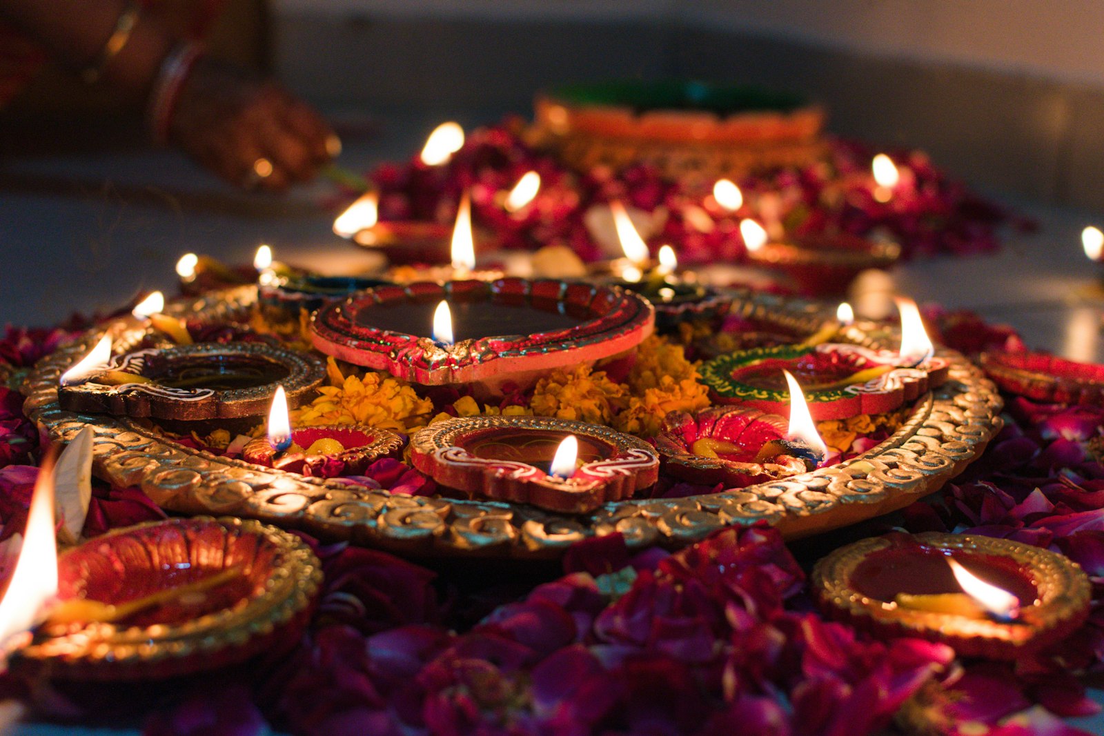 Lit clay oil lamps arranged on an ornate brass tray among scattered pink and magenta flower petals.