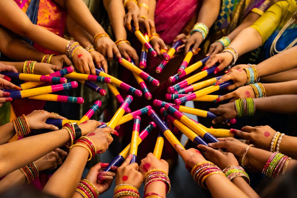 Hands wearing bangles and colourful sleeves meet in a starburst of painted dandiya sticks during a Navratri dance.