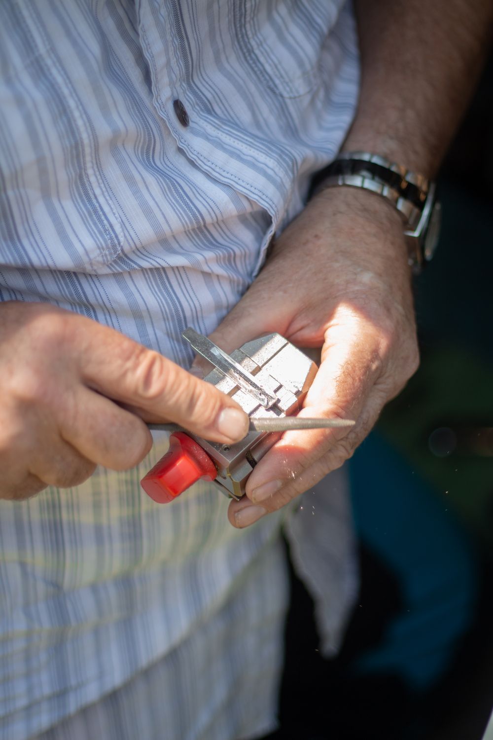 A locksmith's hands filing a key blank clamped in a small vise, with a red handle and fine metal shavings in the air.