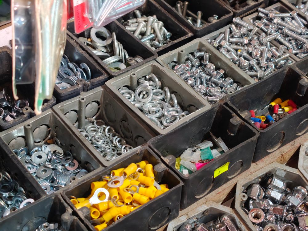 Dark compartment bins sorted with nuts, bolts, washers and small fittings, with a few yellow connectors.