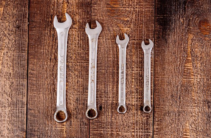 Four metal combination wrenches arranged in a row on a rustic wooden board.