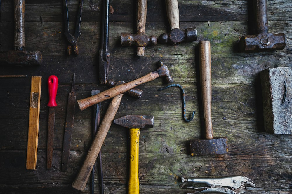 Several old hammers and other hand tools laid out on dark, weathered wooden boards.