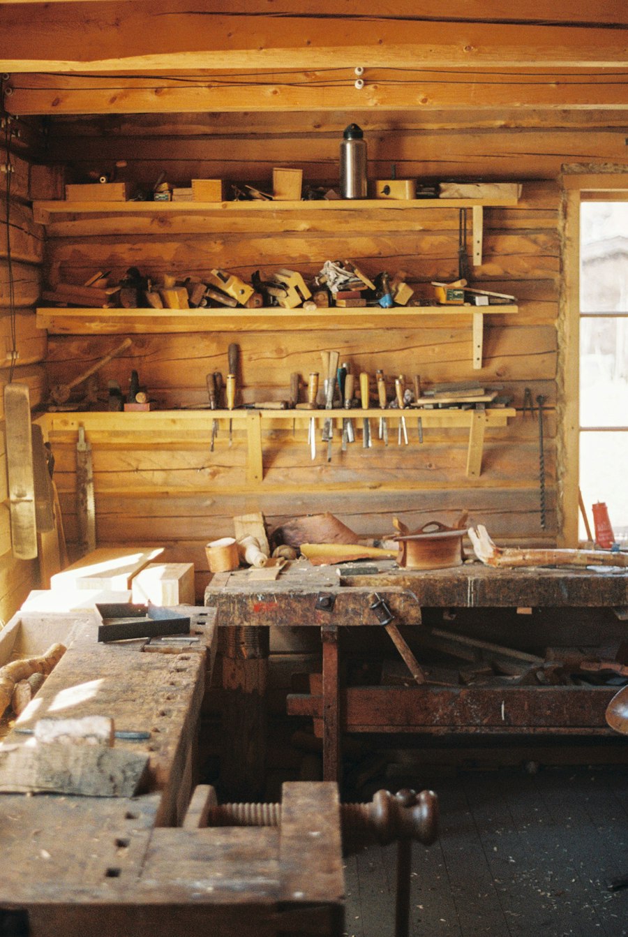 A sunlit wooden workshop with a cluttered workbench and hand tools lined up on shelves above it.