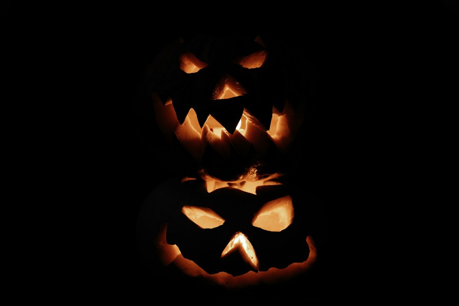 Two carved jack-o'-lanterns stacked one above the other, their jagged grins glowing amber against a pitch-black background.