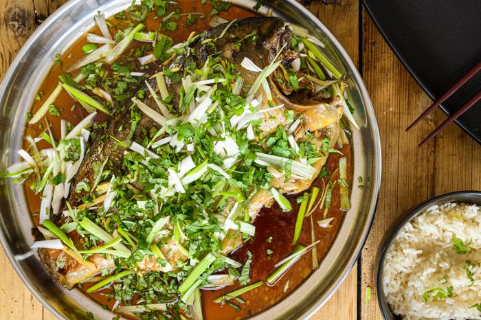 A steamed fish dish garnished with herbs and spring onion, served with rice.