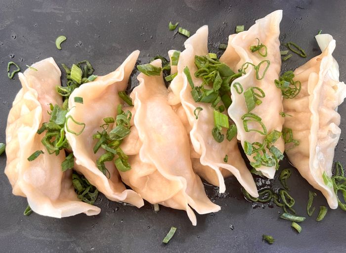 Steamed dumplings garnished with scallions on a dark plate.