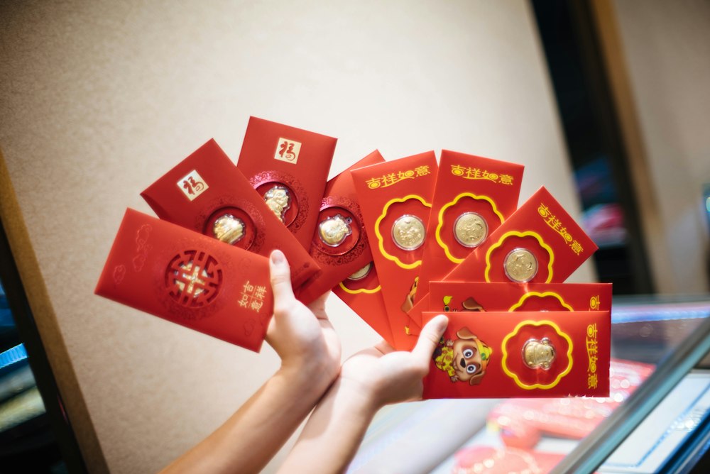 A hand holding a fan of red and gold Chinese red envelopes.
