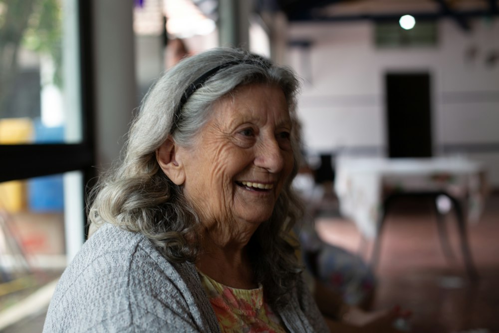 Nani Rosa laughing warmly, grey hair swept back, in a soft grey cardigan and floral top