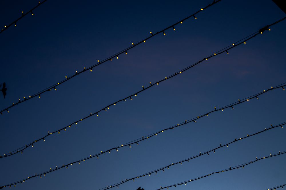 Thin strands of tiny warm lights running diagonally across a deep indigo twilight sky.