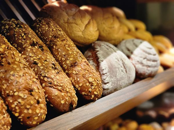 Close-up of oat-topped loaves and floured round breads on a wooden bakery shelf, sharp in front and softly blurred behind.