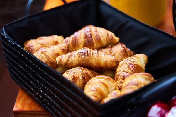 Golden, flaky butter croissants piled in a black woven basket.