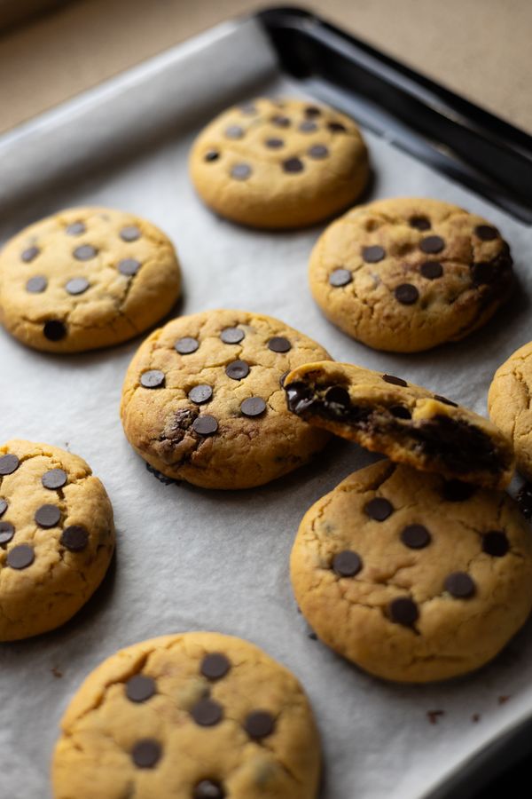 Chocolate chip cookies on a parchment-lined baking tray, one broken open to show the melted chocolate inside.