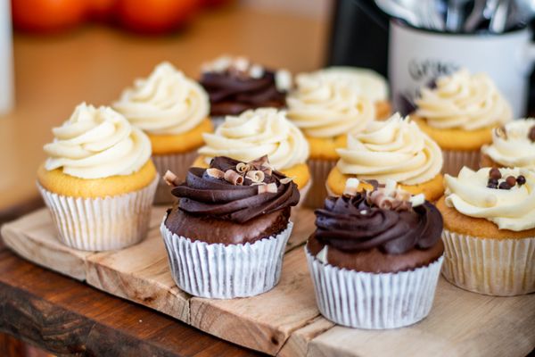 Chocolate and vanilla cupcakes with swirled frosting in paper cases on a rustic wooden board.