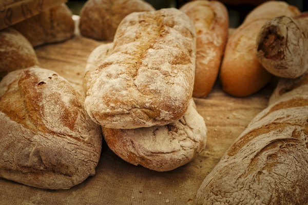 Close-up of golden, flour-dusted loaves and rolls of bread piled together on a rustic cloth.