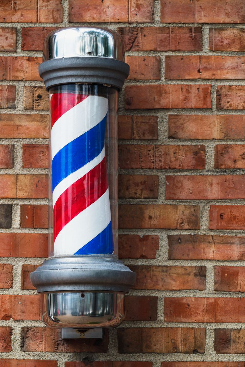 A classic red, white and blue barber pole with chrome caps mounted on a red brick wall.